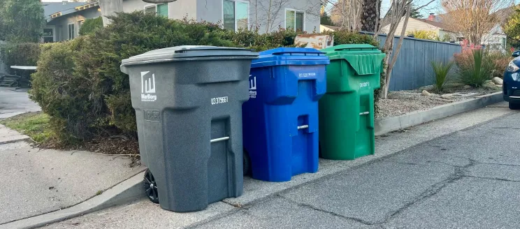 Gray (trash), blue (recycling), and green (yard waste) carts lined up on a street in Santa Barbara