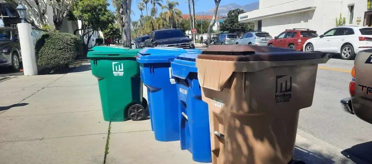 Green, blue, and brown trash carts lined up on the sidewalk.
