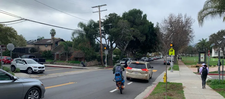 Shows cyclist trying to navigate around school traffic in merge into the travel lane where there is a missing gap in the Cota Street Protected Bike Lane.