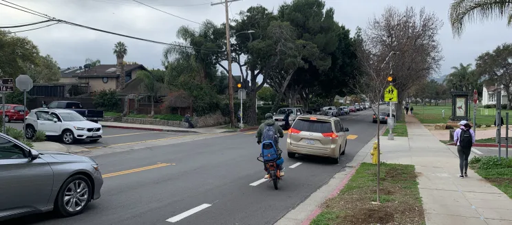 Image shows cyclist trying to navigate around school traffic in merge into the travel lane where there is a missing gap in the Cota Street Protected Bike Lane. La imagen muestra a un ciclista intentando navegar el tráfico escolar para incorporarse al carril de circulación donde falta un hueco en el carril bici protegido de la calle Cota.