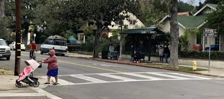 San Andres Street and Anapamu Intersection with people waiting at the bus stop, cyclist in the street and pedestrian in the crosswalk pushing a stroller.