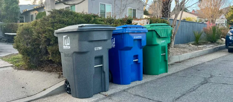 Trash cans on wheels on the curbside.