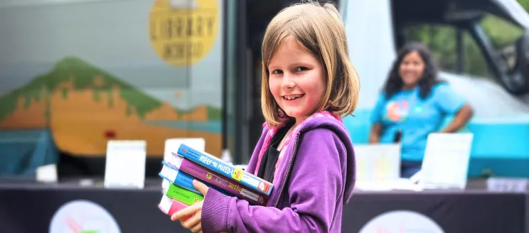 Child smiling while holding books from the Library on the Go Van.
