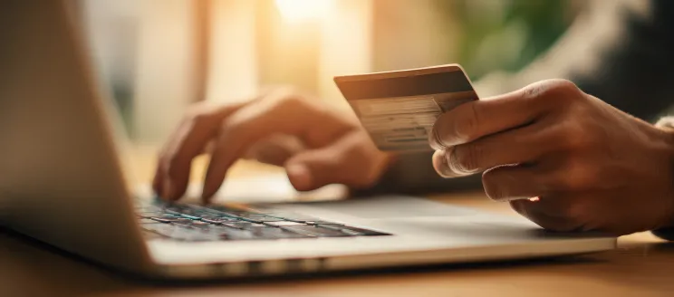 A person holding a credit card in one hand while typing with the other hand on a laptop computer