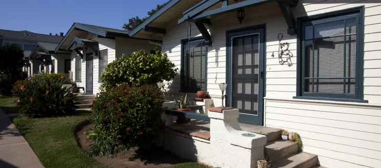 Row of small bungalows with white siding and dark trim.