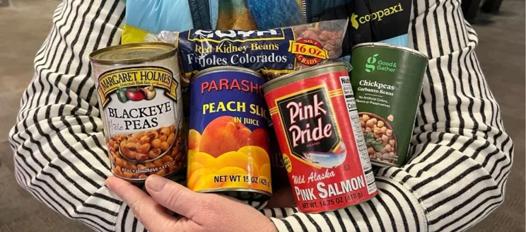 A person in a striped sweater holds assorted canned and packaged food items.