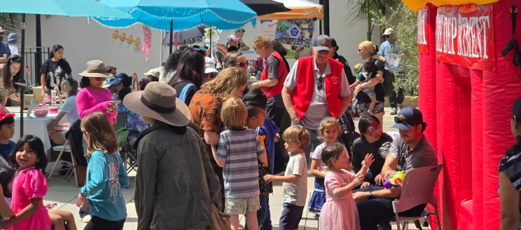 Children and adults gathered for the Children’s Resource Fair with colorful umbrellas and booths on a sunny day.)