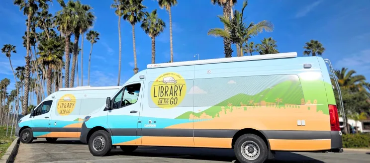 Library on the Go vans parked under tall palm trees on a sunny day with clear blue skies.