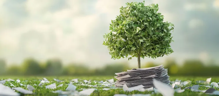 A tree standing on a pile of paper with paper scattered across the surrounding lawn