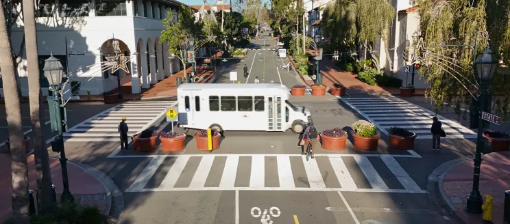 A bus traveling through the Carrillo intersection with pedestrians and cyclists waiting to cross.