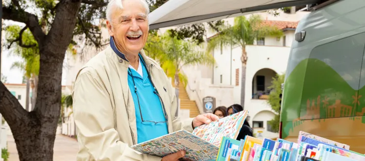 Man browsing books with palm trees and historic buildings in the background