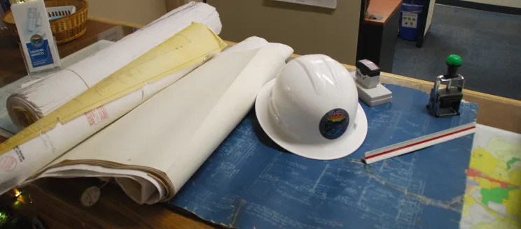 hard hat in a set of plans with a stamp and ruler also in view