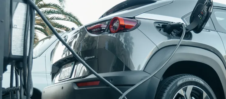 Stock image of grey electric vehicle plugged in to charger