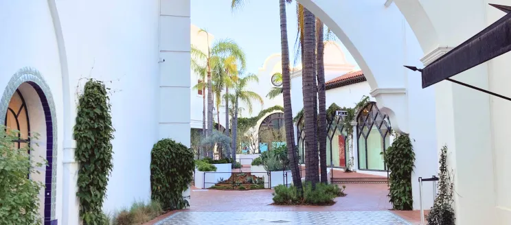 Paseo Nuevo courtyard with white arches, palm trees, and tiled pathways in a serene shopping area.