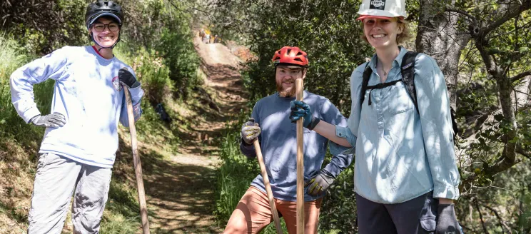 Volunteers on a trail smile while holding tools