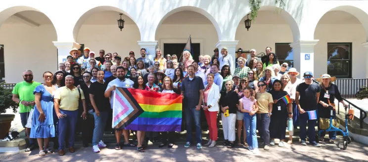 Community members gathered together holding Pride Flags on the steps of City Hall.