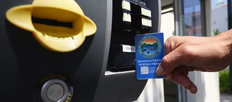 Hand holding a blue Downtown Parking monthly permit card next to a parking payment kiosk.
