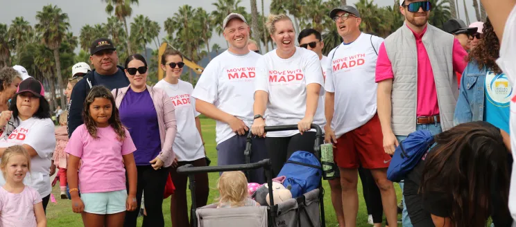 People gathered outdoors on grass, some wearing white 'MADD' shirts, smiling.