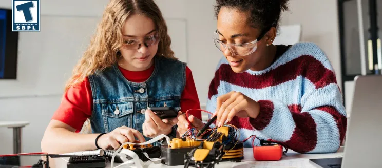 Two teenagers collaborate on assembling a STEM project, focusing on wiring and electronic components.
