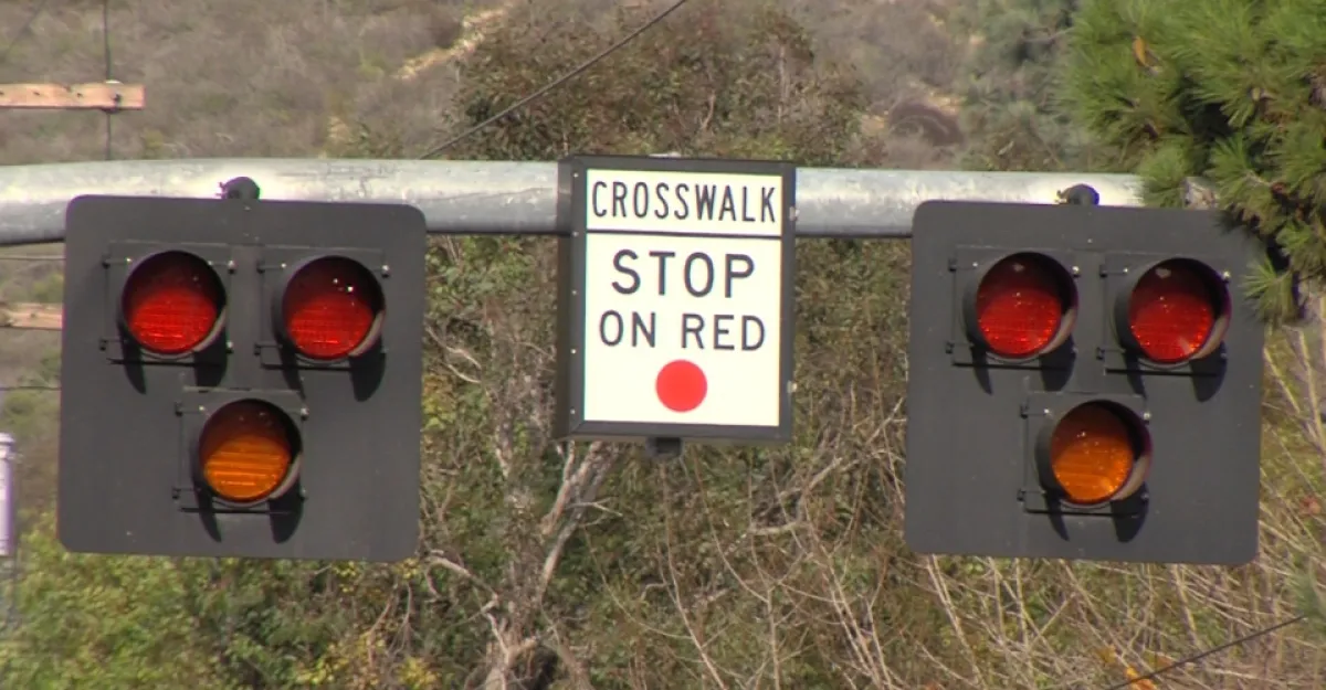 Close up of the signals of a Pedestrian Hybrid Beacon (PHB) with a sign in the center stating, "Crosswalk. Stop on Red."