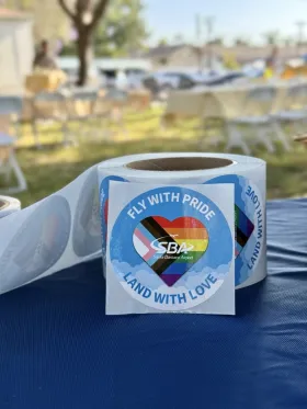 Fly with PRIDE. Land with Love SBA Sticker with the Progress Pride Flag.