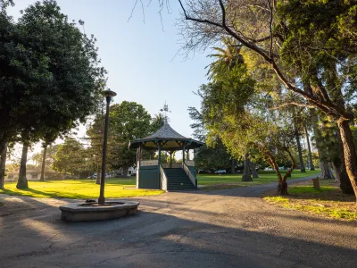 Alameda Bandstand with sun setting in the left of frame, pathways and trees illuminated.