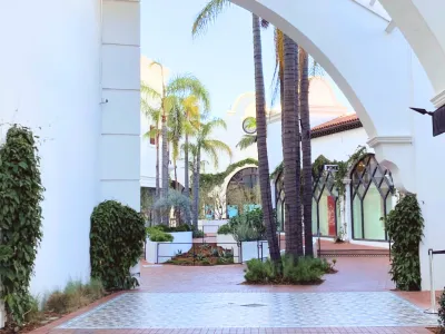 Paseo Nuevo courtyard with white arches, palm trees, and tiled pathways in a serene shopping area.